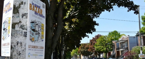 Photo : pancartes verticales du bazar sur un poteau de Limoilou, derrière les arbres verts et rouges d'une avenue de Limoilou.