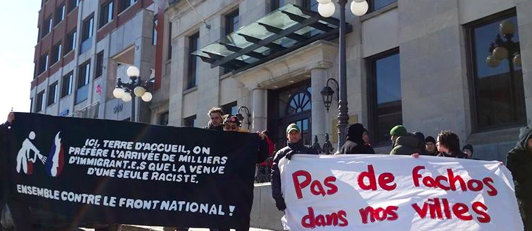 Photo : en centre-ville de Québec devant un hôtel, des gens tiennent deux bannières : 1) Ici, terre d'accueil, on préfère l'arrivée de milliers d'immigrant-es que la venue d'une seule raciste. Ensemble contre le Front national ! 2) Pas de fachos dans nos villes.