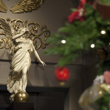 Photo d'une statuette d'un ange aux ailes d'orées. Décoration de Noël floues à côté.