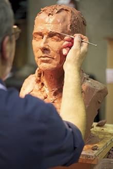 Photo d'un artisan de dos sculptant un buste (tête) d'un homme.
