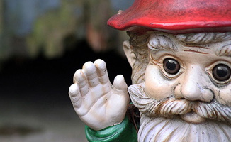 Photo du visage d'un gnome de jardin, soit une petite statuette mignonne d'un gnome, chapeau rouge et yeux bruns sans pupille.