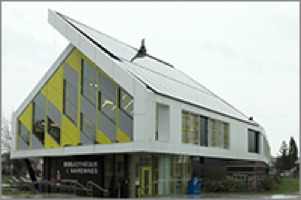 Photo d'une maison triangulaire, dont le toit n'est pas égal, car un côté est un panneau solaire plus large. Les fenêtres ont aussi un motif en triangles, de couleur jaune.