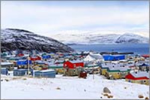 Photo de Salluit, village dans le grand nord. Petites maisons colorées, sur la neige blanche. Montagnes rocailleuses et fleuve très bleu.