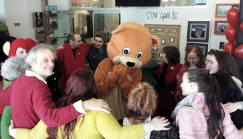 Photo de la 1ère édition : quinzaine de personnes en cercle, bras dessous, bras dessus. Ballons rouges. Mascotte d'ours caramel au milieu. 