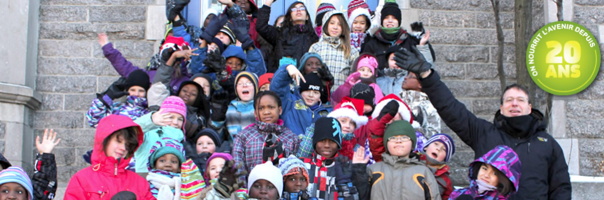 Photo d'une foule d'enfants sur les escaliers du parvis d'une église. Environ 30 enfants souriants, envoyant la main, d'origine diverses, vêtus pour l'hiver. On nourrit l'avenir depuis 20 ans.
