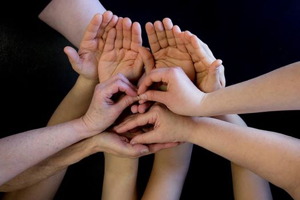 Photo d'une dizaine de mains sur fond noir.  Les mains sont placées collectivement pour représenter un visage.