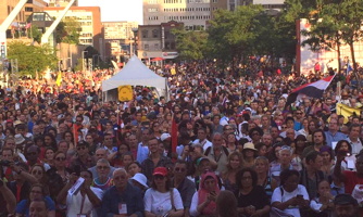 Photo de la foule devant le spectacle d'ouverture du FSM en août 2016. Foule dense et diversifiée. Rayons de soleil sur la ville de Montréal.