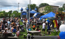 Photo : pique-nique, gazon vert, centaine de personnes, jeux gonflables bleus, tente bleue de la Ville, etc.