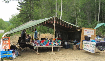 [Photo d'une tente centrale du campement : grande tente ouverte, couvrant les tables pour les vives. Affiches « Non Fracturation », campagne « Vous ne passerez pas », etc.]