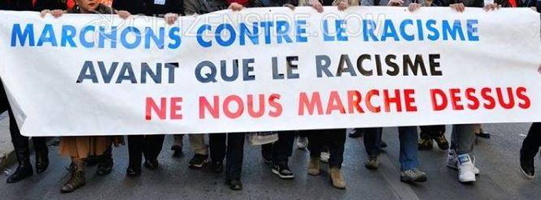 Grande bannière blanche tenue par des gens au devant d'une manifestation, se lisant « Marchons contre le racisme avant le racisme ne nous marche dessus.»