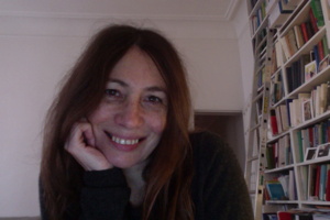 Photo de la conférencière : chez elle, beau sourire, cheveux très long roux-bruns. Librairie débordante derrière elle, avec même une échelle.