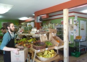 Photo : une épicerie remplie de fruits et légumes. Une jeune homme aux cheveux longs attachés transporte une boîte.