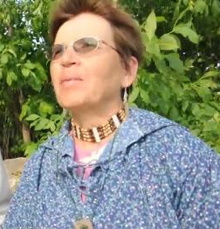 Photo de Marie-Émilie Lacroix, regardant devant à l'horizon. Cheveux courts roux, collier autochtone, chemise mauve-bleu fleurie.