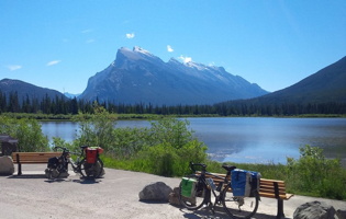 Photo : grandes montagnes rocailleuses, lac bleu, ciel très bleu, vélos le long de bancs extérieurs.