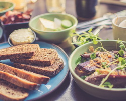 Photo qui accompagne l'annonce : quelques petites « toasts » sur une assiette bleue ; petit plat avec des légumes et tofu grillé ; et autres aliments hors focus.