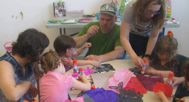 Photo : trois adultes (deux femmes, un homme) aident quatre fillettes qui bricolent.