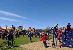 Parc avec des jeux, plusieurs enfants sur les jeux et adolescents en vélo. Beau ciel bleu dégagé.