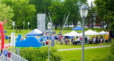 Photo d'une des fêtes familiales passées sur ce parc : chapiteaux, jeux pour enfants de couleur bleu, gazon vert, beaucoup de gens debouts autour.