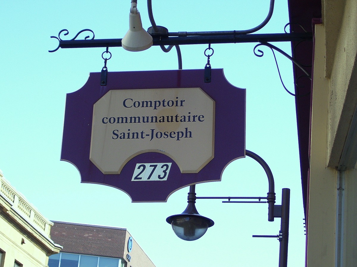 Photo de l'écriteau réelle: Comptoir communautaire Saint-Joseph - 273. On apperçoit derrière le bâtiment du Centre Jacques-Cartier près de la Biblio. Gabrielle-Roy