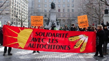 [PHOTO: d'une bannière rouge lors d'une manif : Solidarité avec les autochtones. Dessin jaune d'un demi-soleil.]