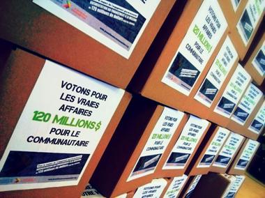 Photo : vue de près de boîtes avec des messages dessus, tel : Votons pour les vraies affaires : 120 millions pour le communautaire.