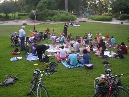 Photo : pique-nique sur le gazon vert du parc. Il y a environ 40 personnes ; quelques vélos.