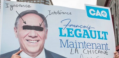 Affiche tenue bien haut qui est en fait une affiche électorale de François Legault mais modifiée avec les mots Ignorance, Intolérance, La chicane.