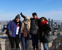 Photo: quatre adultes, côte à côte, vêtus pour l'hiver. Derrière, une grande ville plus bas, au soleil. Semblent être trois femmes et un homme. Elles/il viennent de pays d'Amérique du Sud.