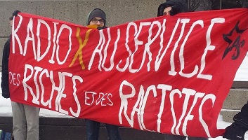 Trois jeunes hommes tiennent une grande bannière rouge : « Radio X au service des riches et des racistes ».