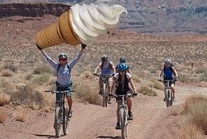 Photo de cyclistes traversant une zone désertique, style sud des États-Unis ou Mexique, mais un énorme cône de crème glacée est ajoutée au-dessus des mains de la première cycliste.