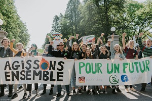 Photo : deux bannières au devant d'une manifestation à Québec tenues par des adolescent.es pour la plupart. Styles divers et bras levés. « Agissons ensemble ... pour un futur »