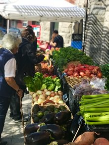 Photo de gens, de dos, regardant les tables couvertes de légumes divers, dont une dame âgée.       