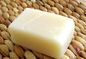 Simple barre de savon de forme classique, mais de couleur un peu plus beige que blanc, placée sur un tapis de paille.