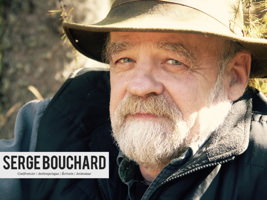 Portrait de Serge Bouchard : regard sympathique, chapeau beige contre le soleil, barbe blanche, manteau d'automne.