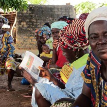 Photo : une dizaine de femmes africaines attendent sur un banc commun. Leurs tuniques et foulards sont de plusieurs couleurs et motifs.