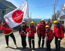 Photo du départ de Cacouna en avril 2016: six femmes portant une veste rouge, casquette jaune, et un grand drapeau blanc avec un cercle rouge de la Marche Innu Meshkenu.