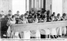 Photo ancienne de jeunes filles autochones dans une école catholique. Sous-titre: Le temps d'étude à l'école résidentielle Natale, (Le Fort) la Résolution, NWT. Crédit: biblio. et Archives le Canada, ID PA-042133.