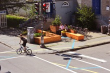 Photol : un jeune en vélo au coin de la rue St-Joseph : il y a des beaux bancs en bois aux côtés de l'église Jacques-Cartier.